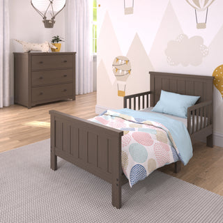 A toddler’s bedroom with a gray wooden bed, pastel bedding, Child Craft’s Harmony 3-Drawer Dresser with Changing Table Topper in Brushed Truffle, light wood flooring, mountain and hot air balloon decals on the wall, and a large rug.