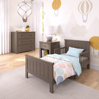 A cozy child’s bedroom includes the Child Craft Harmony 3-Drawer Dresser with Changing Table Topper in Brushed Truffle, light wood furniture, a bed with balloon-patterned bedding, hot air balloon decals on white walls, and a window with white curtains.