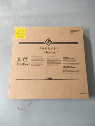 A large brown box labeled Child Craft sits on a gray surface. It likely contains a Hampton Toddler Bed, Matte White, with guard rails. The box features warnings, instructions in multiple languages, and a yellow sticker in the top left corner.