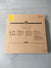 A large brown box labeled Child Craft sits on a gray surface. It likely contains a Hampton Toddler Bed, Matte White, with guard rails. The box features warnings, instructions in multiple languages, and a yellow sticker in the top left corner.
