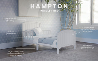 The Child Craft Hampton Toddler Bed in Matte White features shiplap paneling, a slatted headboard and footboard, built-in guard rails, an arched design, sturdy wood construction, and a low profile for easy access.