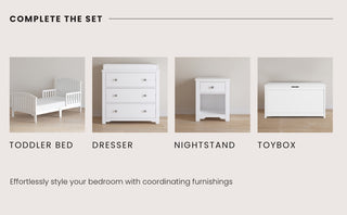 Four white bedroom pieces are shown: the Child Craft Hampton Toddler Bed in Matte White with guard rails, a dresser, nightstand, and toy box. All have a classic design and are set against a beige wall and wood floor. The bed is low for safety.