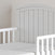 A close-up of the Child Craft Hampton Toddler Bed in Matte White shows vertical slats, an arched headboard, and secure guard rails, ready for use as a toddler bed against a light-colored wall.