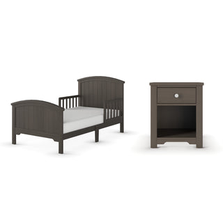 The Child Craft Hampton Toddler Bed in Dapper Gray features sturdy guard rails and includes a crib mattress. It sits next to a matching nightstand with one drawer and an open shelf, both showcasing a simple, classic design.