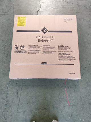 A large brown cardboard box labeled Child Craft sits on a gray floor. The box may contain a Hampton Toddler Bed, Dapper Gray, and features safety warnings, handling instructions, plus a bright yellow label in the upper left corner.