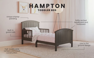 The Child Craft Hampton Toddler Bed in Dapper Gray features a softly arched headboard and footboard, shiplap paneling, built-in guard rails, quality pine veneer, fits a standard crib mattress, and sits low to the ground.