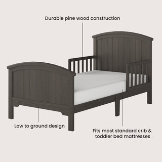The Child Craft Hampton Toddler Bed in Dapper Gray features a curved headboard and footboard, slatted side rails, sturdy guard rails, and a low-profile design. Made from durable pine, it fits any standard crib mattress for safe toddler sleep.