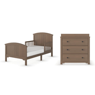 The Child Craft Hampton Toddler Bed in Dusty Heather features simple panel designs, rounded edges, half-height side rails, and a white mattress, paired with a matching three-drawer light brown dresser.
