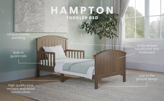 The Child Craft Hampton Toddler Bed in Dusty Heather features built-in guard rails, an arched headboard and footboard, unique shiplap paneling, and a low-to-the-ground design—perfect for softly lit rooms with light green walls and a window.