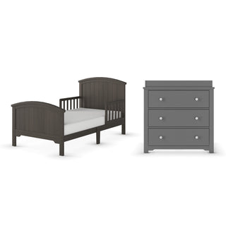 The Child Craft Hampton Toddler Bed in cool gray with low guard rails and a white mattress sits next to a matching three-drawer dresser, both showcasing a simple, modern design.