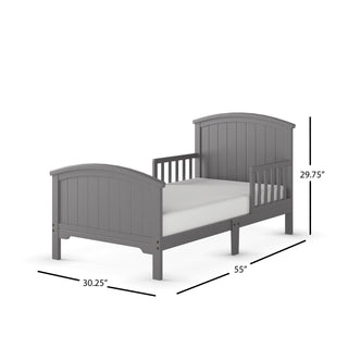The Child Craft Hampton Toddler Bed in Cool Gray features a slatted headboard, footboard, guard rails, and a low-to-ground design for safety. Mattress included. Dimensions: 55" L x 30.25" W x 29.75" H.