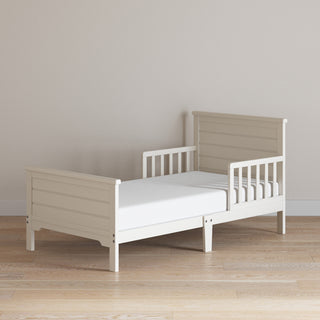 The Child Craft Woodland Toddler Bed in Brushed Cotton features sturdy toddler bed rails on both sides, standing on a light wooden floor against a plain beige wall.
