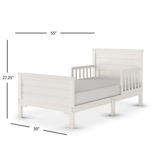 The Child Craft Woodland Toddler Bed in Brushed Cotton features a white wooden modern farmhouse style with slatted headboard, footboard, and toddler rails. Measures 55"L x 30"W x 27.25"H and includes a mattress on the bed frame.