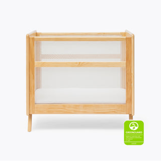 The HALO Mini Breathable Mesh Crib, featuring light wood, mesh sides, and a white mattress, is displayed against a plain background with a Greenguard Gold certification badge in the bottom right corner.