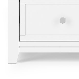 Close-up of the bottom left corner of the Atwood 4-Drawer Chest by Child Craft in matte white, featuring a hexagonal silver knob and clean modern lines—a minimalistic dresser ideal for nurseries or baby furniture.