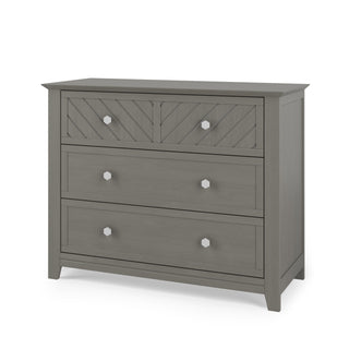 The Child Craft Atwood 3-Drawer Dresser in Lunar Gray features a chevron-patterned top drawer with two knobs, plain lower drawers, and angled legs. The flat top is ideal for adding a baby changing table topper.
