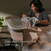 A woman places a swaddled baby into a HALO BassiNest® Swivel Sleeper 4.0 Air with Dreamweave Breathable Pad, featuring a patented lowering wall for easier access, next to a bed. Text reads: Patented Lowering Wall. Easier Access.
