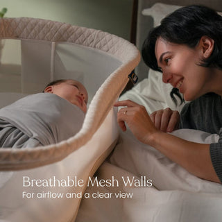 A smiling woman leans over a bed, gently touching a baby’s hand as the baby rests in the HALO BassiNest® Swivel Sleeper 4.0 Air with Dreamweave Breathable Pad. Text reads: Breathable mesh walls for airflow and a clear view.