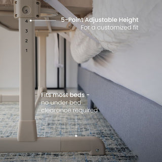 Close-up of the HALO 2-in-1 Bedside Bassinet Sleeper rail with labeled features like a 5-point adjustable height bar and a base fitting under most beds—ideal for use as a bassinet or bedside sleeper next to a bed with a white blanket.