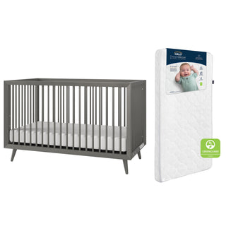 The Child Craft Cranbrook 2-Piece Crib and DreamWeave Set in Lunar Grey includes a convertible crib and breathable mattress, both featuring a white package with a smiling baby label and Greenguard certification for non-toxic materials.