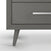 Close-up of the bottom corner of the Cranbrook Double Dresser in Lunar Gray by Child Craft, featuring angled legs and a sleek silver drawer handle—a stylish addition to any nursery furniture set.