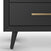 Close-up of the Child Craft Cranbrook Double Dresser in Ebony shows an angled leg and a drawer with a gold horizontal handle. Set against a white background, this modern nursery piece features a sleek, minimalistic design.