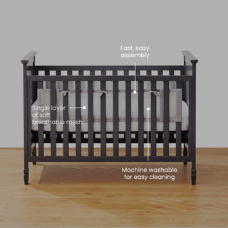 A HALO Breathable Mesh Crib Liner for Full Sized Solid End Crib with a black finish is shown on a wooden floor against a gray background. It ensures infant safety with easy assembly, breathable mesh for comfort, and machine washable parts for simple cleaning.