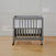 A gray HALO mini crib with wheels sits on a wooden floor against a white wall, featuring the Breathable Mesh Crib Liner for comfort and airflow. Its designed with crib safety in mind, easy to assemble, and machine washable for effortless cleaning.
