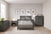 A modern bedroom features gray wooden furniture, including a bed, dresser, nightstand, and the Denman 4 Drawer Chest by Child Craft in Midnight Gray. Decor includes botanical art, a plant, a lamp, neutral walls, and light wood floors.