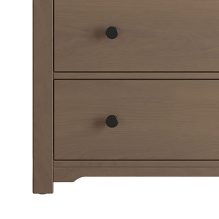 A close-up of the Child Craft Harmony 3-Drawer Dresser with Changing Table Topper in Dusty Heather shows two drawers with round black knobs, a light brown finish, and short square legs—perfect for nursery storage or pairing with the included topper.