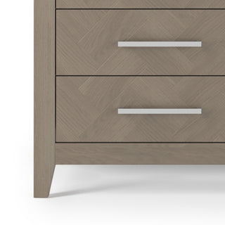 Close-up of the Child Craft Kieran 6-Drawer Double Dresser in Crescent Gray, featuring a herringbone pattern, sleek silver handles, and angled legs—ideal for a nursery—shown against a white background.