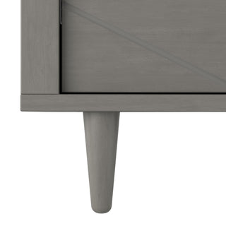 Close-up of the bottom left corner of the Child Craft Surrey Hill 3 Drawer Dresser in Lunar Gray, showing a leg and diagonal front panel design—ideal for modern nurseries.
