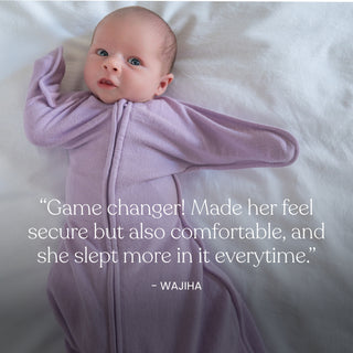 A baby in a lavender HALO SwaddleStretch™ Newborn Swaddle TOG 0.5 lies on a white bed, with a quote below from Wajiha praising the swaddle for its comfort and for helping her baby sleep better.