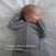 A baby rests on a white blanket in a grey HALO SwaddleStretch™ Newborn Swaddle TOG 0.5 with distinct long sleeves, one sleeve-covered hand near their mouth. Text reads: Unique sleeve design. For self-soothing.