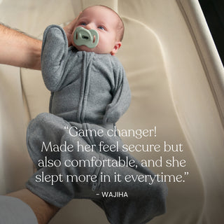 A baby in a gray zip-up onesie lies in a bassinet with a pacifier. Text overlay: “Game changer! The HALO SwaddleStretch™ Newborn Swaddle made her feel secure yet comfy, and she slept more in it every time.” – Wajiha.