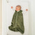A baby sleeps peacefully on their back in a white crib, wearing the HALO Wearable Blanket Plushy Dot Velboa TOG 1.5 in soft green, with outstretched arms and a front zipper for comfort.