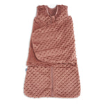 The HALO Swaddle Plushy Dot Velboa TOG 3.0 is a soft, pinkish-brown sleeveless sleep sack with textured raised dots, a front zipper, and an attached adjustable swaddle wrap for a cozy 3-in-1 sleep solution.