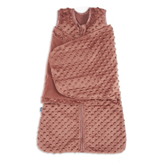 The HALO Swaddle Plushy Dot Velboa TOG 3.0 is a soft, pinkish-brown sleeveless sleep sack with textured raised dots, a front zipper, and an attached adjustable swaddle wrap for a cozy 3-in-1 sleep solution.