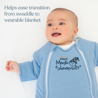 A smiling baby on a white surface wears the HALO Baby Merlin’s Magic Sleepsuit® 100% Cotton, designed to ease swaddle transition and support restful sleep during regressions.