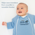 A smiling baby on a white surface wears the HALO Baby Merlin’s Magic Sleepsuit® 100% Cotton, designed to ease swaddle transition and support restful sleep during regressions.