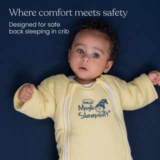 A curly-haired baby in a yellow Baby Merlin's Magic Sleepsuit® 100% Cotton by HALO lies on navy blue. Where comfort meets safety—designed for safe back sleeping and perfect for swaddle transition. Features the HALO logo.