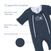 The HALO Baby Merlin's Magic Sleepsuit® 100% Cotton in dark blue is a cozy baby sleep aid with callouts of three layers: soft cotton outer, 100% cotton lining, and plush polyfill core. Text reads 