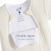 A close-up of the cream-colored HALO Baby Merlin's Magic Sleepsuit® 100% Cotton shows two open zippers, a white tag reading 