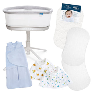 The HALO Smart Bassinet Bundle includes a white bassinet on a stand, a blue Bamboo SleepSack Swaddle, two patterned baby bibs, two white mattress pads, and packaging featuring a smiling baby.