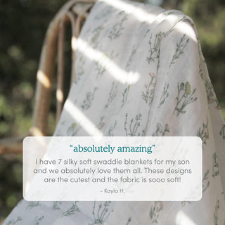 A boutique silky soft swaddle blanket 3 pack by aden + anais, featuring delicate floral patterns and bamboo-infused viscose, drapes over a wooden chair. In a white text box, a customer praises the silky softness and cute designs.