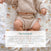 A baby in a beige knit outfit sits on a white aden + anais Disney™ Winnie the Pooh boutique 100% cotton muslin swaddle blanket, decorated with small colorful rainbows, with a customer review shown at the bottom of the image.