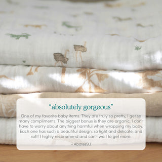 Two soft, folded aden + anais organic cotton muslin swaddle blankets with animal and nature prints are stacked on a table. A review praises their organic material, delicate design, versatility, softness, and safety for babies.