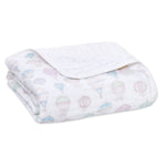 The aden + anais organic cotton dream blanket is a folded white muslin featuring pastel hot air balloon illustrations. GOTS certified, it’s soft, lightweight, and ideal for babies or as charming decor.