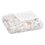 The aden + anais boutique silky soft muslin dream blanket showcases a whimsical nature-inspired design with cozy brown animal and plant illustrations on one side and a silky soft white background with small yellow patterns on the reverse.