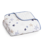 The aden + anais boutique cotton muslin dream blanket features folded white cotton muslin with blue edging and a pattern of blue, beige, and gray stars. Its breathable fabric ensures comfort and coziness for a perfect nights sleep.